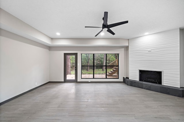 unfurnished living room with ceiling fan, a textured ceiling, a fireplace, and light hardwood / wood-style floors