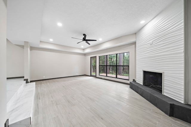 unfurnished living room featuring ceiling fan, a fireplace, light hardwood / wood-style flooring, and a textured ceiling