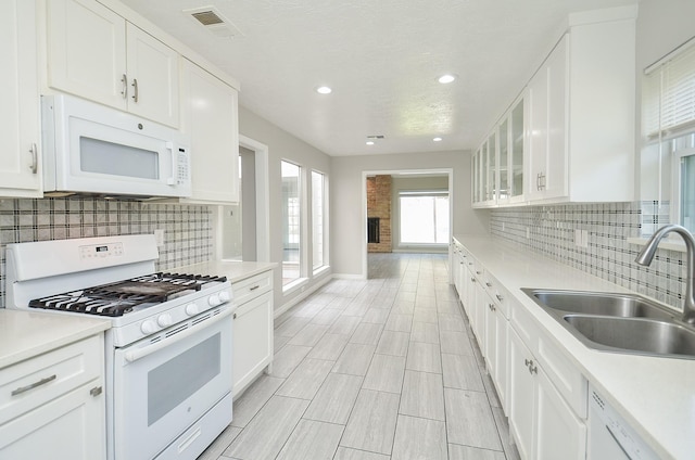 kitchen featuring white appliances, a sink, white cabinets, light countertops, and glass insert cabinets