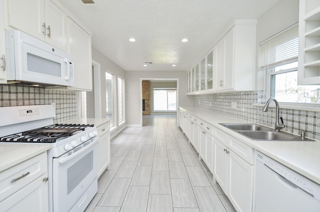 kitchen with white appliances, a sink, white cabinetry, light countertops, and glass insert cabinets