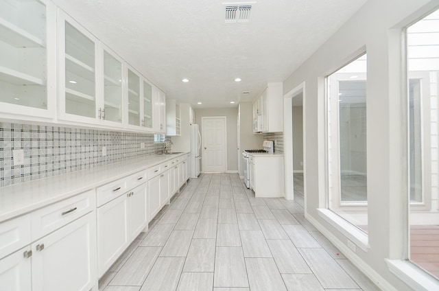 kitchen featuring glass insert cabinets, white appliances, white cabinetry, and visible vents