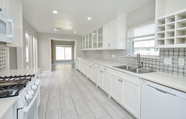 kitchen featuring white appliances, white cabinets, glass insert cabinets, light countertops, and a sink