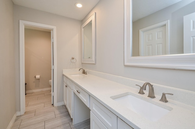 bathroom featuring double vanity, wood finish floors, a sink, and toilet