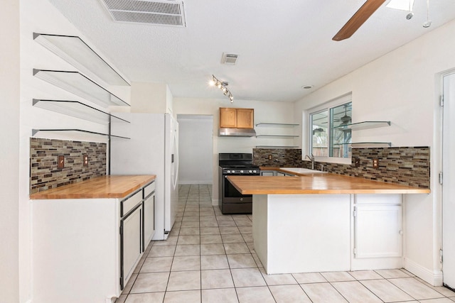 kitchen featuring sink, butcher block countertops, light tile patterned floors, stainless steel range with gas stovetop, and kitchen peninsula