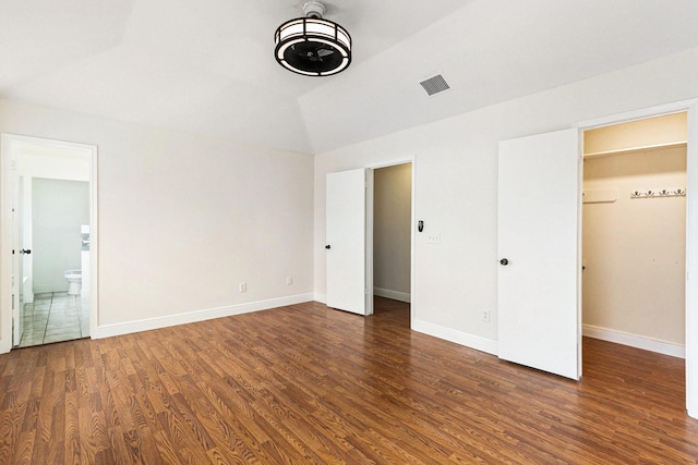 unfurnished bedroom with dark wood-type flooring, a walk in closet, lofted ceiling, and ensuite bath