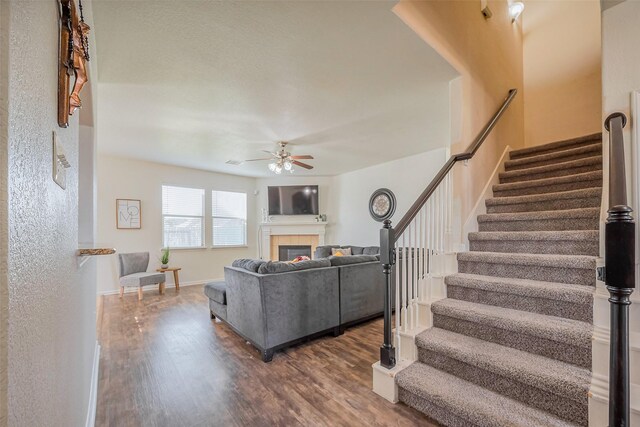 living room with wood finished floors, stairway, baseboards, ceiling fan, and a tile fireplace