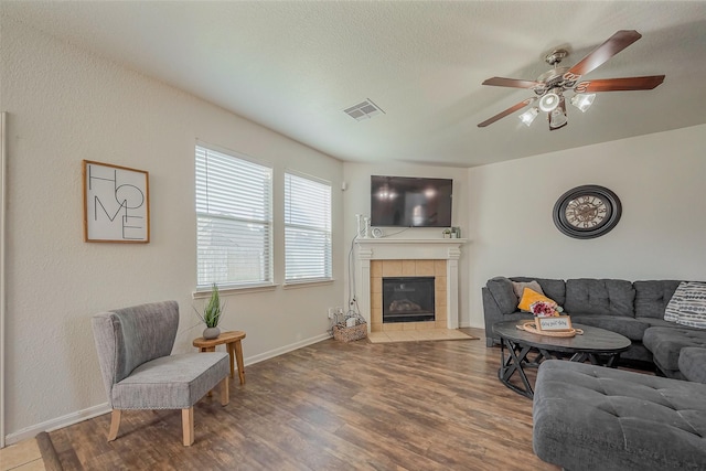 living area featuring visible vents, a tile fireplace, baseboards, and wood finished floors