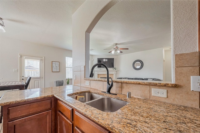 kitchen with light stone countertops, brown cabinets, arched walkways, a sink, and open floor plan