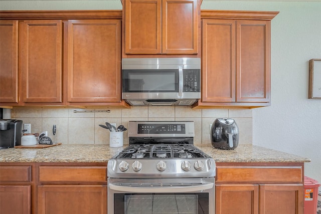 kitchen featuring light stone counters, stainless steel appliances, brown cabinetry, and decorative backsplash