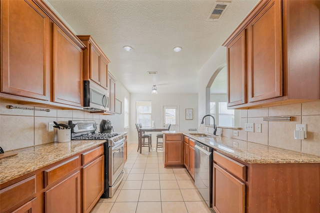 kitchen with a sink, appliances with stainless steel finishes, brown cabinetry, and light tile patterned floors