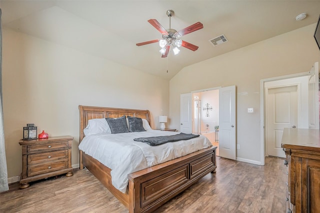 bedroom featuring wood finished floors, visible vents, baseboards, lofted ceiling, and ensuite bathroom