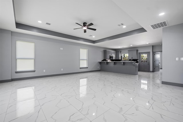 unfurnished living room with ceiling fan and a tray ceiling