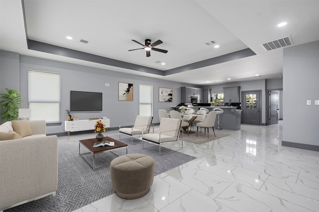 living room with ceiling fan and a tray ceiling