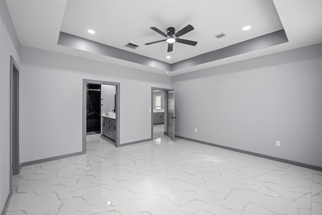 unfurnished bedroom featuring ceiling fan, ensuite bathroom, and a tray ceiling