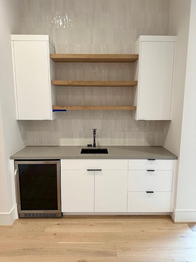 bar featuring wine cooler, light wood-type flooring, sink, and white cabinets