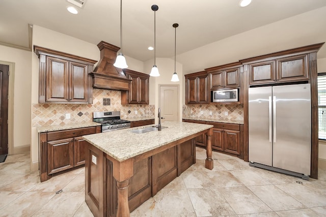 kitchen featuring premium range hood, appliances with stainless steel finishes, sink, a kitchen island with sink, and light stone counters