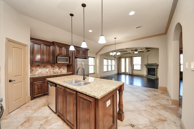 kitchen with pendant lighting, sink, appliances with stainless steel finishes, a kitchen island with sink, and light stone countertops