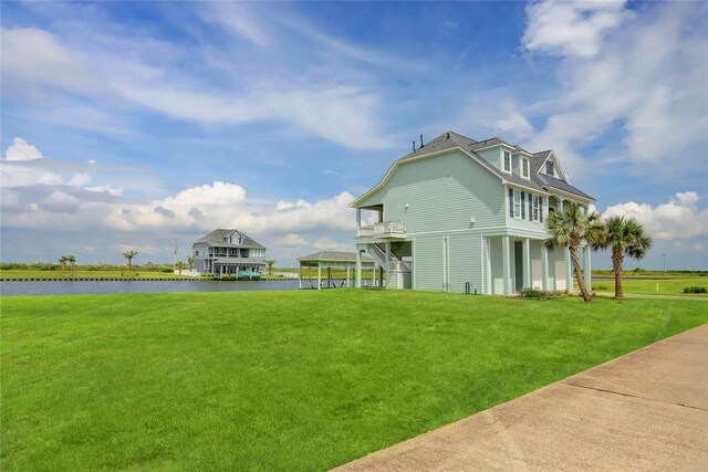 rear view of property featuring a garage, a balcony, a water view, and a yard