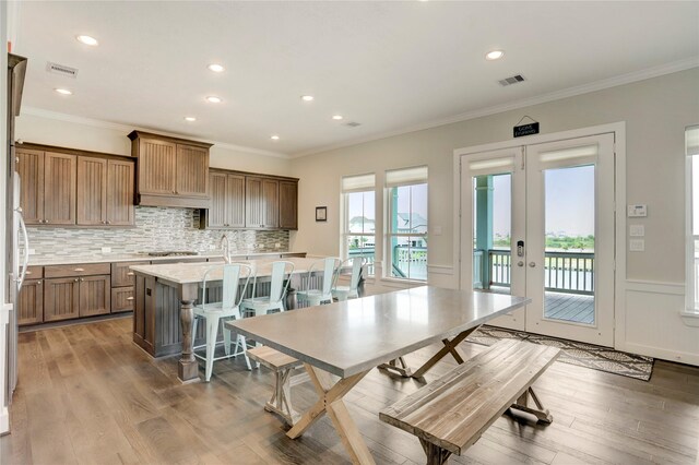 kitchen with crown molding, a center island with sink, wood-type flooring, a kitchen bar, and french doors