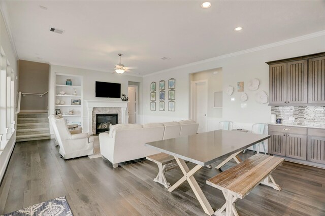 dining space with wood-type flooring, ornamental molding, built in features, and ceiling fan