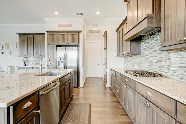 kitchen featuring appliances with stainless steel finishes, sink, light stone counters, crown molding, and light hardwood / wood-style flooring