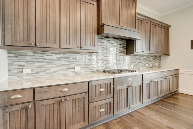 kitchen with stainless steel gas stovetop, custom exhaust hood, ornamental molding, and light stone counters