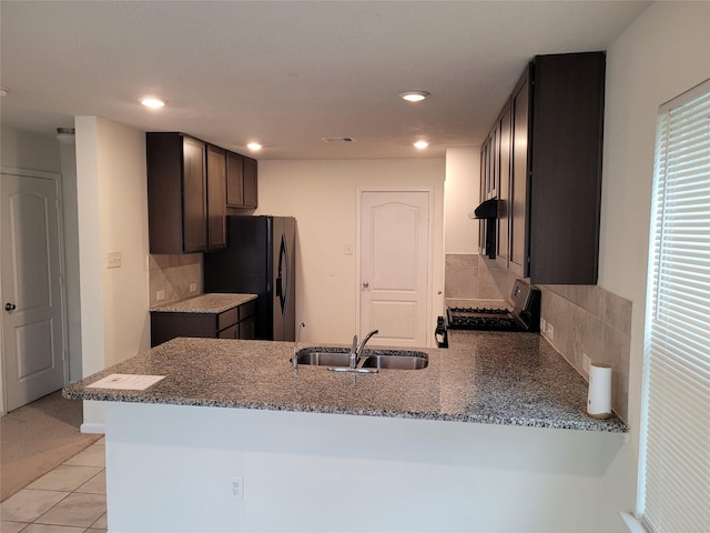 kitchen with black fridge with ice dispenser, a peninsula, range with gas cooktop, a sink, and stone counters