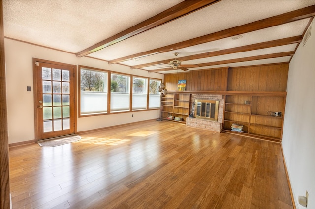 unfurnished living room featuring a fireplace, beamed ceiling, ceiling fan, a textured ceiling, and light hardwood / wood-style flooring