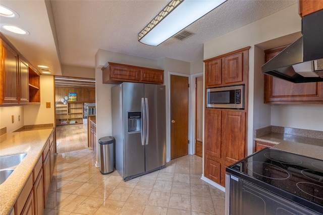 kitchen featuring wall chimney range hood, light tile patterned floors, sink, stainless steel appliances, and a textured ceiling