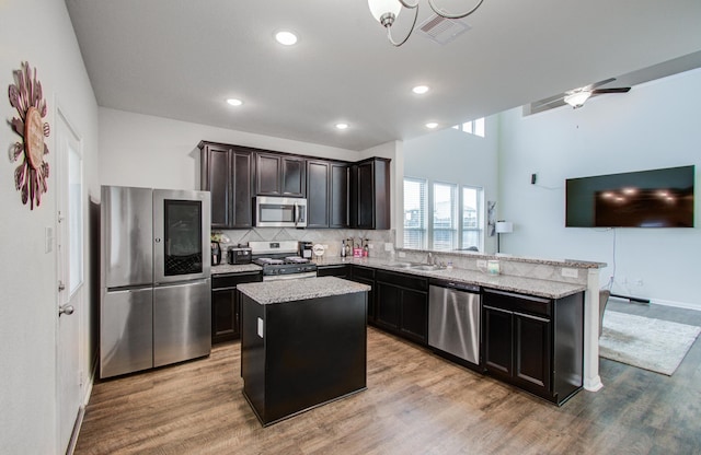 kitchen with appliances with stainless steel finishes, sink, decorative backsplash, a center island, and light wood-type flooring