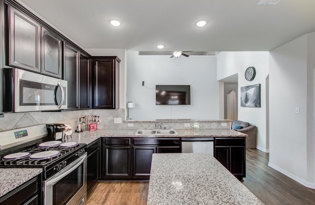 kitchen with sink, light wood-type flooring, appliances with stainless steel finishes, light stone countertops, and backsplash