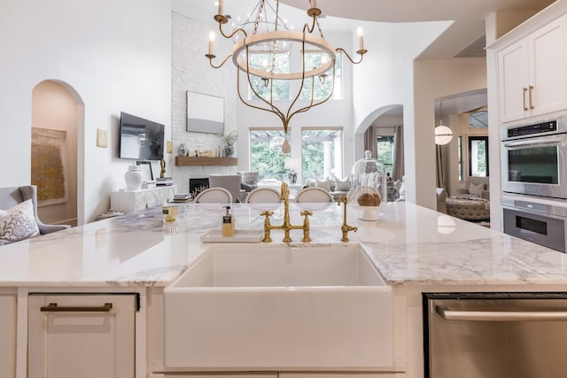 kitchen featuring light stone counters, an island with sink, a sink, appliances with stainless steel finishes, and open floor plan