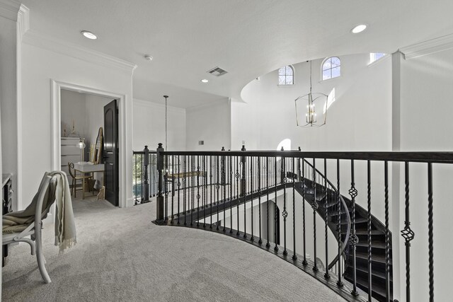 hallway featuring carpet, visible vents, ornamental molding, an upstairs landing, and a chandelier