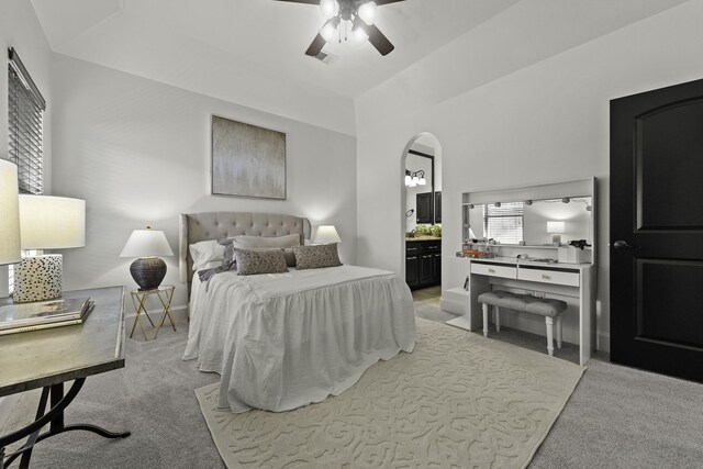 carpeted bedroom with arched walkways, ceiling fan, ensuite bath, and baseboards