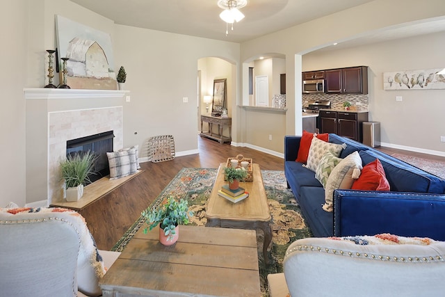 living room with ceiling fan, dark hardwood / wood-style flooring, and a tiled fireplace