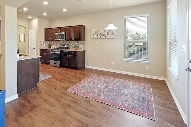 kitchen featuring stainless steel appliances, pendant lighting, light wood-type flooring, and decorative backsplash