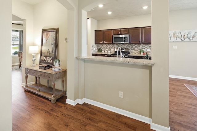 kitchen with hardwood / wood-style flooring, stainless steel appliances, dark brown cabinetry, light stone countertops, and decorative backsplash