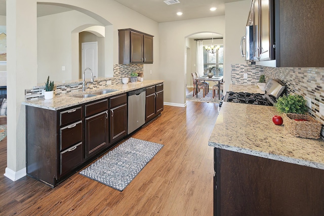 kitchen with appliances with stainless steel finishes, sink, light stone counters, dark brown cabinets, and light wood-type flooring