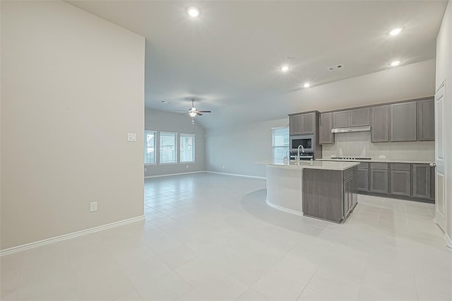 kitchen with lofted ceiling, sink, black cooktop, a center island with sink, and stainless steel microwave