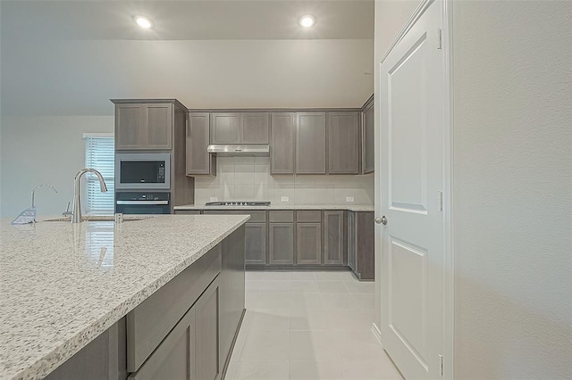 kitchen featuring light stone counters, stainless steel gas cooktop, built in microwave, decorative backsplash, and oven