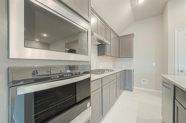 kitchen featuring gray cabinetry, stainless steel appliances, light stone countertops, light tile patterned flooring, and vaulted ceiling