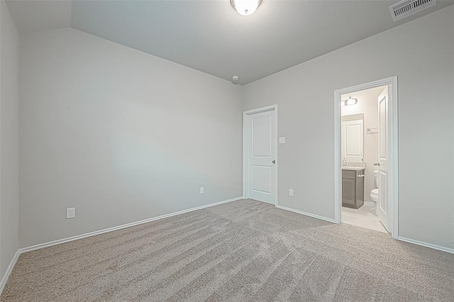 unfurnished bedroom featuring light colored carpet, ensuite bathroom, and lofted ceiling