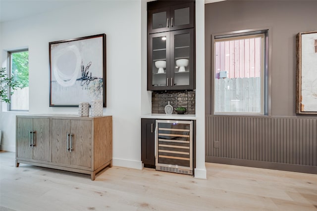 bar featuring backsplash, wine cooler, light wood-style floors, a bar, and baseboards