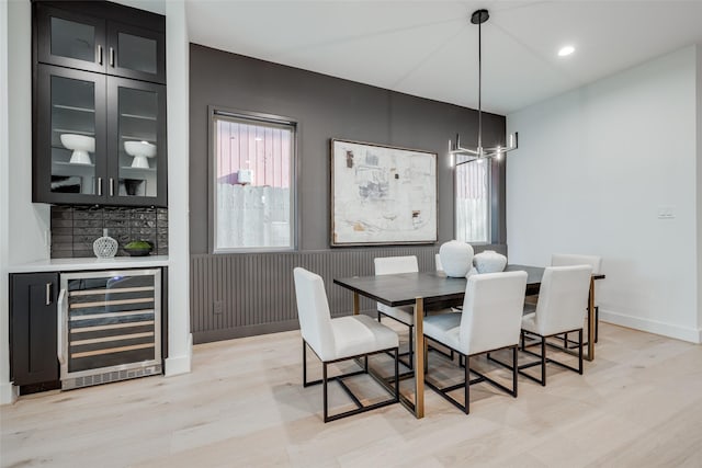 dining space featuring a bar, wine cooler, baseboards, and light wood finished floors