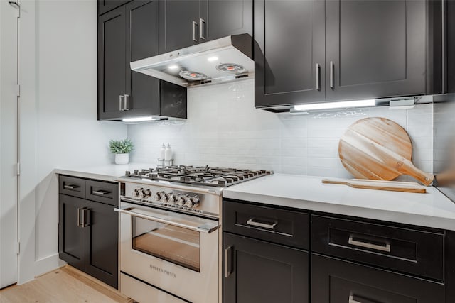 kitchen featuring backsplash, under cabinet range hood, light countertops, dark cabinetry, and high end range