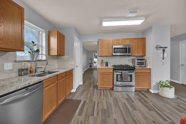 kitchen with sink, tasteful backsplash, hardwood / wood-style flooring, stainless steel appliances, and light stone countertops