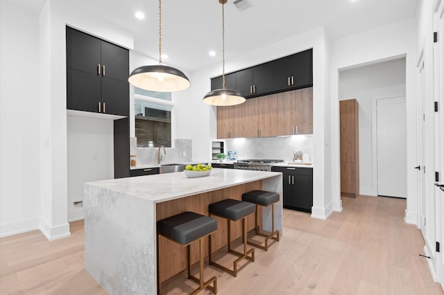 kitchen featuring a breakfast bar, sink, decorative light fixtures, light hardwood / wood-style flooring, and a kitchen island