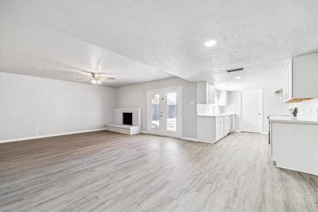 unfurnished living room featuring light hardwood / wood-style flooring, ceiling fan, a textured ceiling, a brick fireplace, and french doors