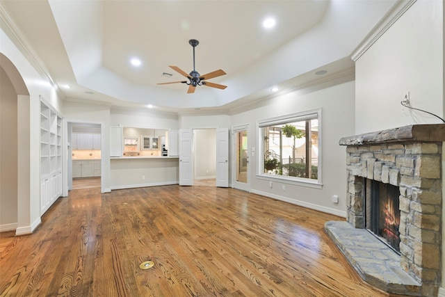 unfurnished living room with crown molding, hardwood / wood-style floors, a stone fireplace, and a raised ceiling