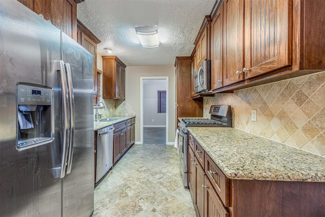 kitchen featuring sink, appliances with stainless steel finishes, light stone counters, a textured ceiling, and decorative backsplash